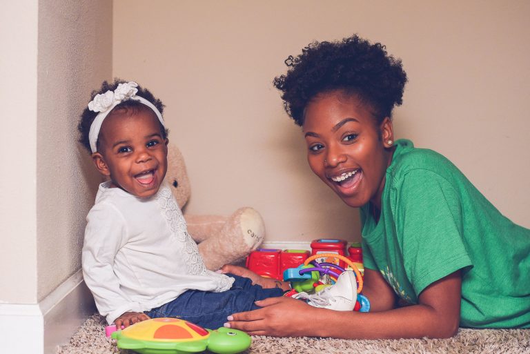 Adorable baby and sitter playing. Both are looking at camera smiling and laughing.