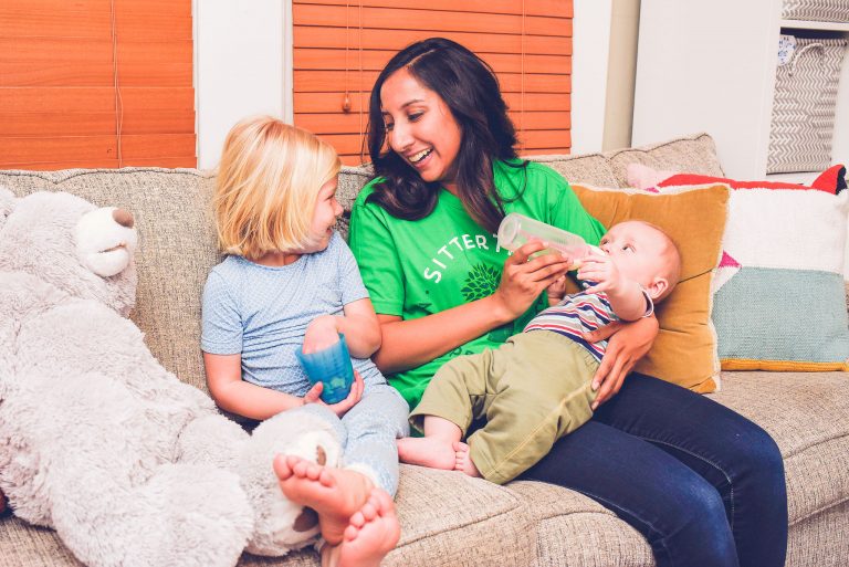 Sitter feeding baby a bottle while talking to toddler