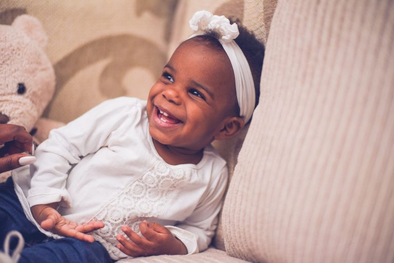 Smiling baby girl with a white bow making eye contact