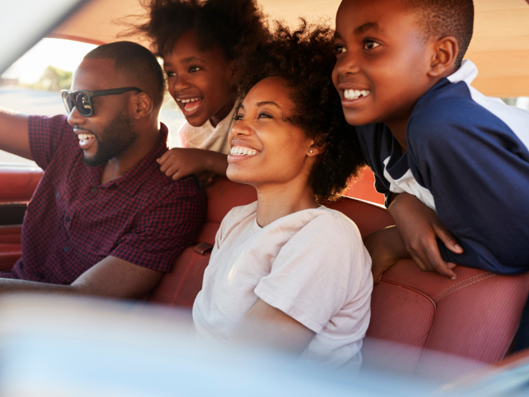 Day Trips from Nashville: Smiling family of four inside a car, ready for a road trip. Two children are leaning forward with excitement, while the parents are seated in the front, looking ahead with smiles.