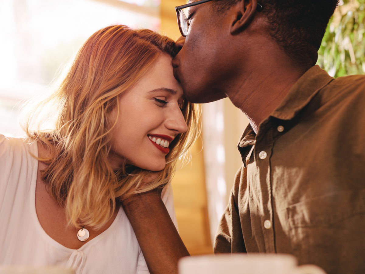 Date night ideas in Charlotte: A romantic moment between a couple at a cafe, with the man gently kissing the woman's forehead as she smiles, enjoying the intimate atmosphere.