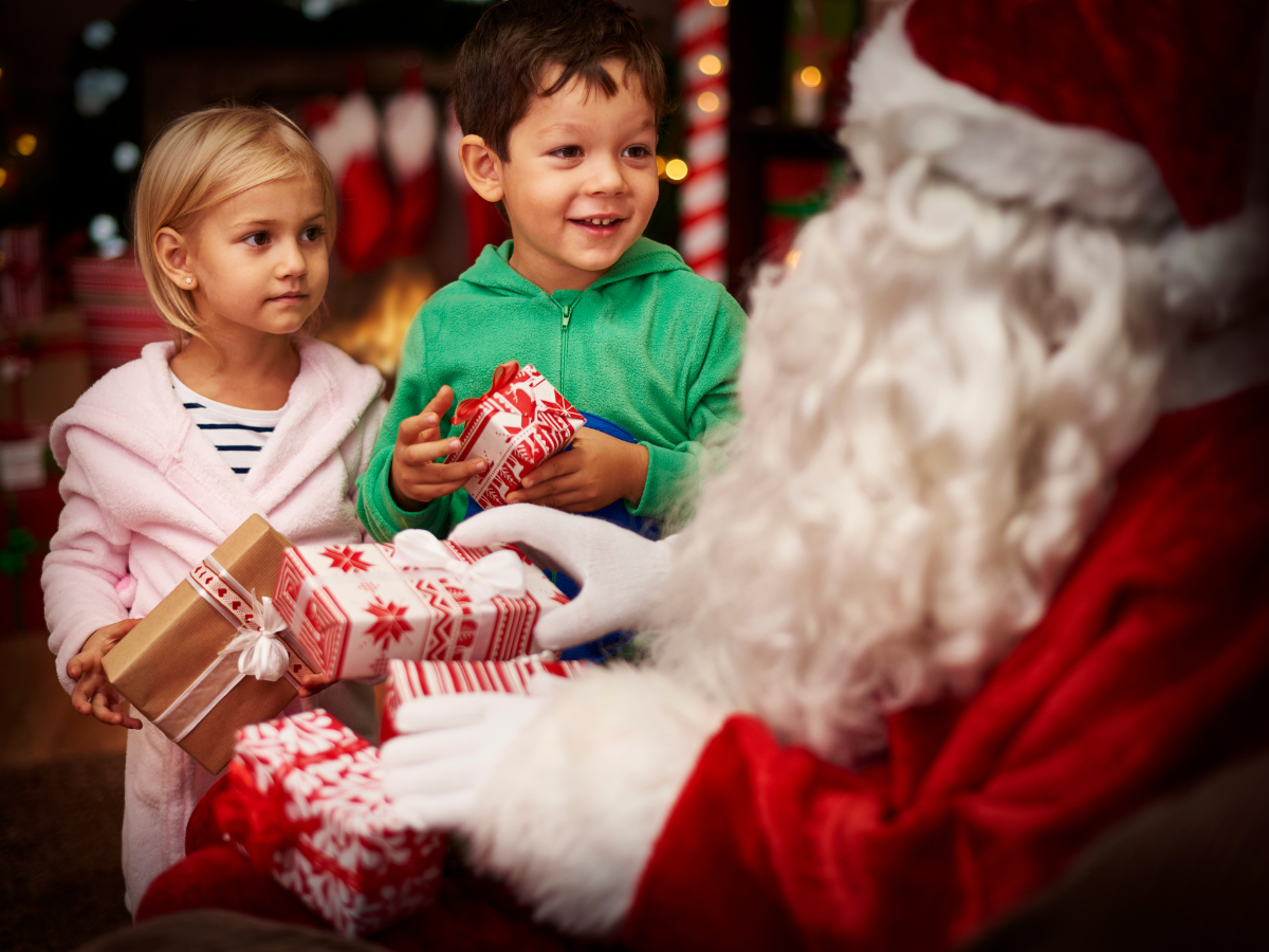 Photos with Santa in San Antonio: Two young children receiving wrapped gifts from Santa Claus, with holiday decorations in the background