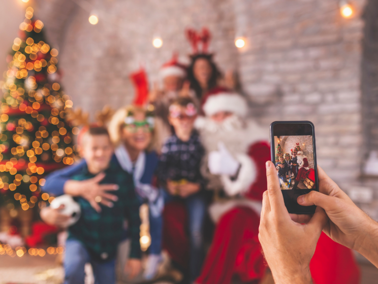 Photos with Santa in Orlando: A person taking a photo of a family posing with Santa Claus in a festive, decorated room with a Christmas tree and lights in the background