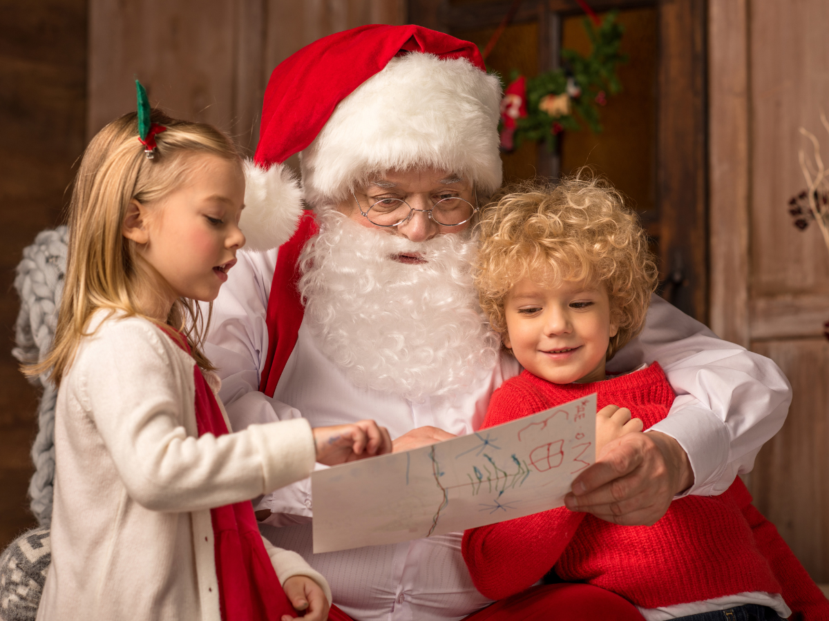 Photos with Santa in Denver: Santa Claus reading a Christmas list with two smiling children, one girl and one boy, in a cozy holiday setting