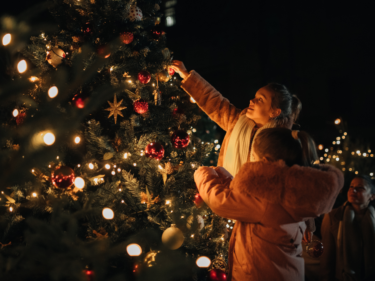 Photos with Santa in Washington, DC, for 2024: A family decorating a brightly lit Christmas tree outdoors at night, with warm golden lights and red ornaments creating a festive holiday atmosphere