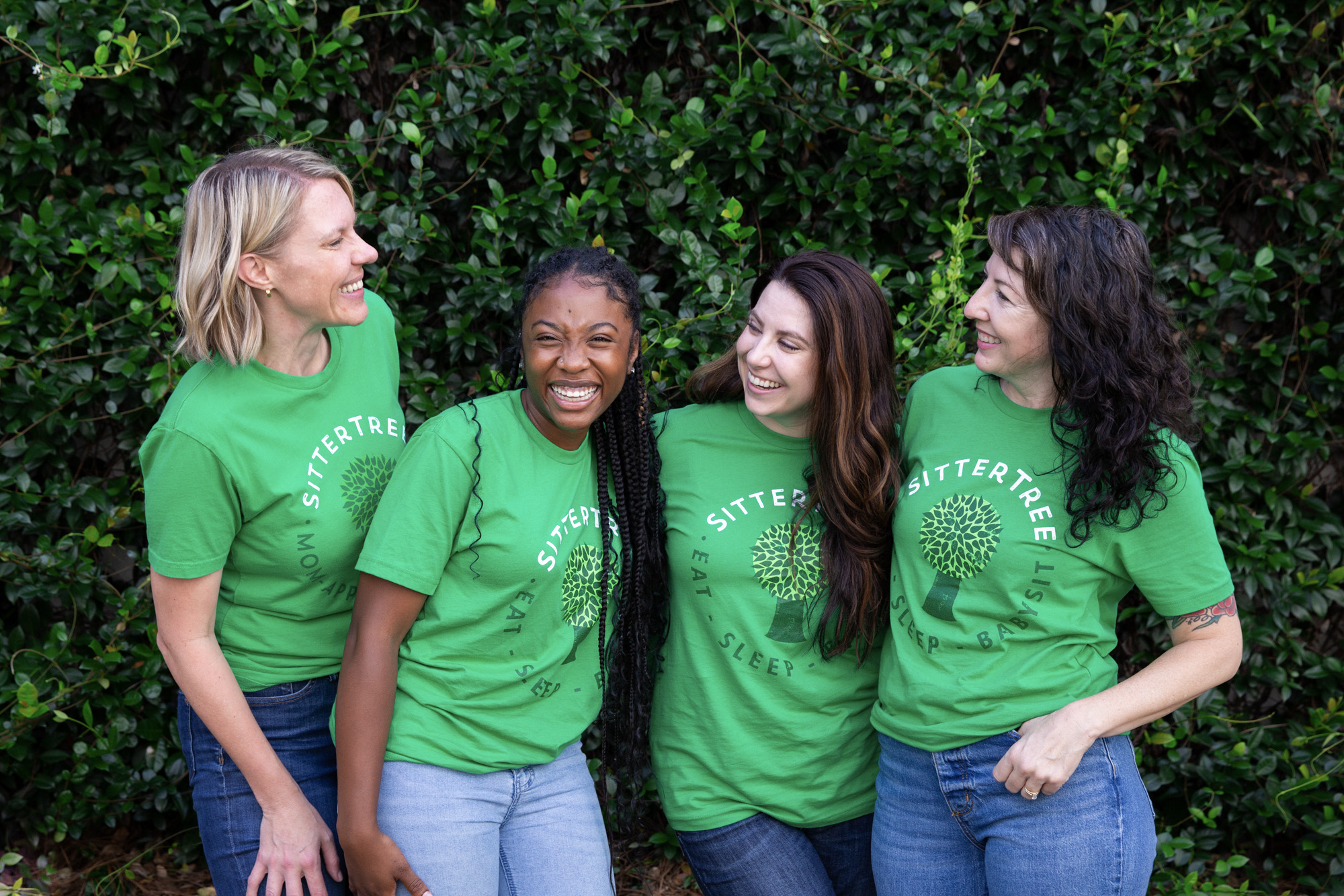 The Best Babysitter Apps and Websites to Hire a Babysitter: Four smiling women wearing green SitterTree t-shirts standing outdoors in front of lush greenery, enjoying a lighthearted moment together