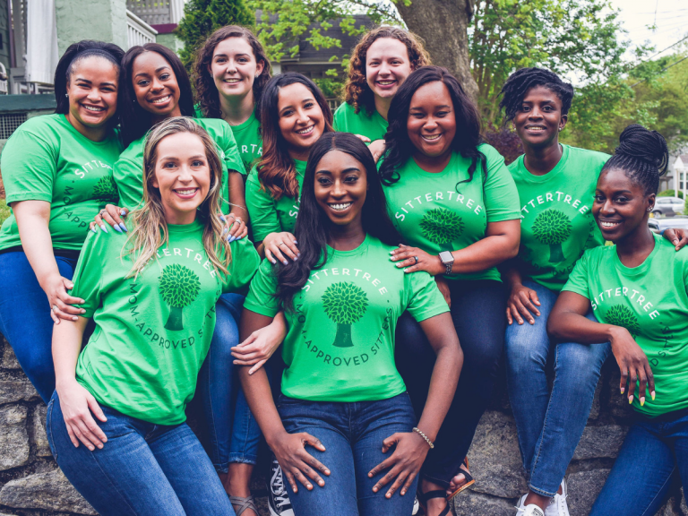 How to gain babysitting experience: A group of smiling SitterTree sitters wearing green 'Mom-Approved Sitter' T-shirts, sitting together outdoors, showcasing community and trust