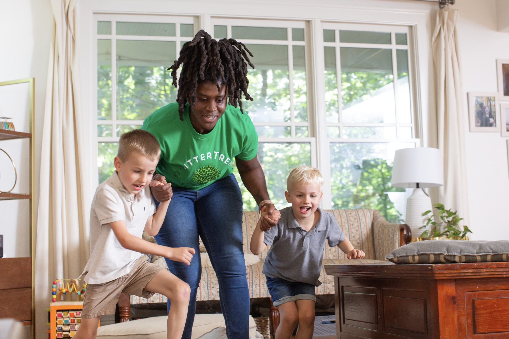 A babysitter wearing a green SitterTree t-shirt playing energetically with two young boys in a bright and cozy living room: How to ace a babysitting interview