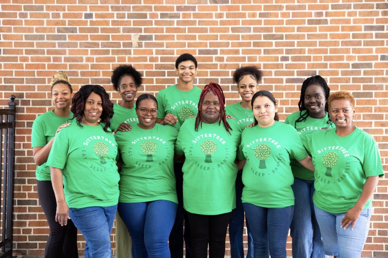 A group of nine individuals wearing matching green SitterTree t-shirts, standing in front of a brick wall and smiling at the camera: Best babysitting apps and websites