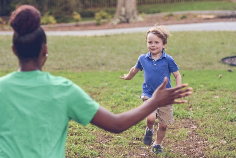 Young boy running toward a babysitter with open arms in a grassy outdoor setting, capturing a joyful and playful moment: fun babysitting games