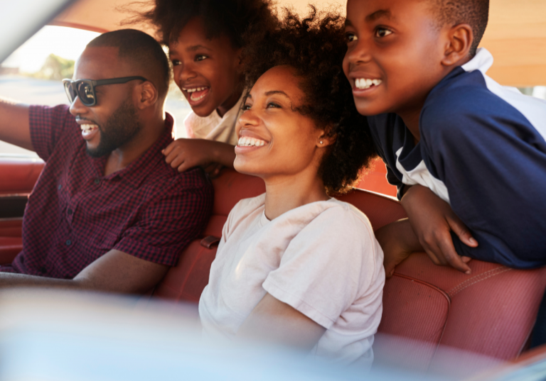 Day Trips from Nashville: Smiling family of four inside a car, ready for a road trip. Two children are leaning forward with excitement, while the parents are seated in the front, looking ahead with smiles.