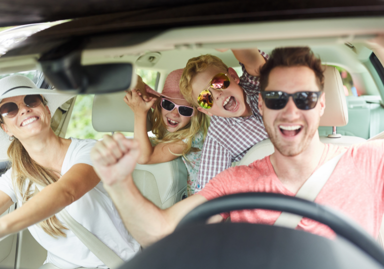 Day trips from Nashville: Happy family of four smiling and cheering inside a car, wearing sunglasses and hats, enjoying a fun road trip together.