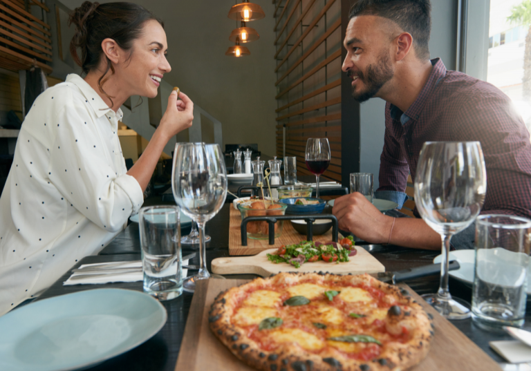 date night ideas near me: couple on a date night eating pizza and drinking wine