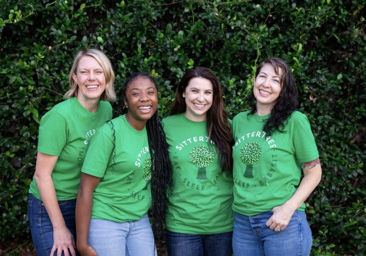 A group of four smiling babysitters wearing green SitterTree t-shirts stand in front of a lush green hedge, showcasing camaraderie and team spirit: How to become a babysitter