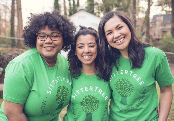 Three smiling babysitters wearing green SitterTree t-shirts standing close together outdoors, showcasing their camaraderie and joyful expressions in a natural setting: Setting Minimum Hours for Babysitting